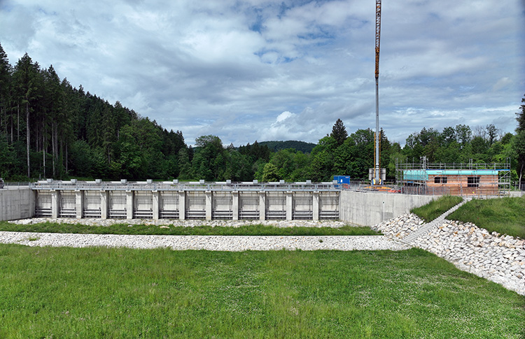 Drohnenaufnahme des Hochwasserrückhaltebeckens Feldolling. In der Bildmitte ist das Einlassbauwerk zu sehen, direkt daneben die Baustelle des neuen Betriebsgebäudes.